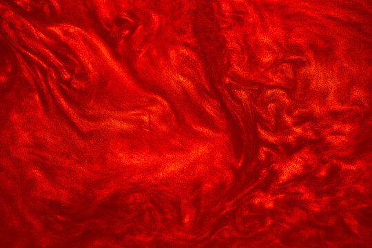 Shimmering red abstract background. Liquid glitter paint texture waves and swirls. Beautiful shiny red glitter texture. Metallic paint close-up as a holiday background.