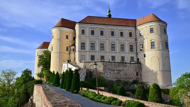 A baroque hilltop castle with round towers above a path lined with evergreens, Mikulov, Czech Republic