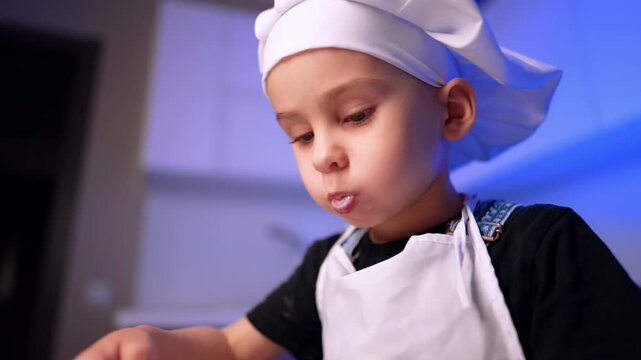 Close portrait of child in white toque with milk residue around mouth. Soft blue background light highlights a young face during mealtime indoors.