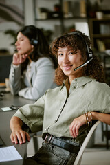 Obraz na płótnie Canvas Portrait of diverse young adult female call center agents working in office wearing headsets. Image suitable for customer service training and corporate communication, vertical
