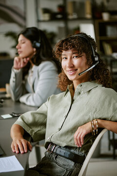 Portrait of diverse young adult female call center agents working in office wearing headsets. Image suitable for customer service training and corporate communication, vertical