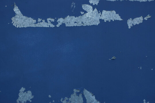 Close-up of peeling blue paint on weathered metal, revealing a rough silvery surface underneath