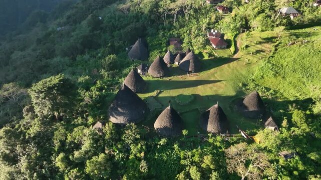 Aerial view of the traditional cone-shaped houses of Waerebo Village nestled in the lush green mountains of Satar Mese Barat, East Nusa Tenggara, Indonesia.