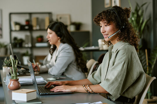 Diverse young adult female operators wearing headsets working on laptops in call center. Image suitable for customer support, telemarketing, and corporate communication campaigns