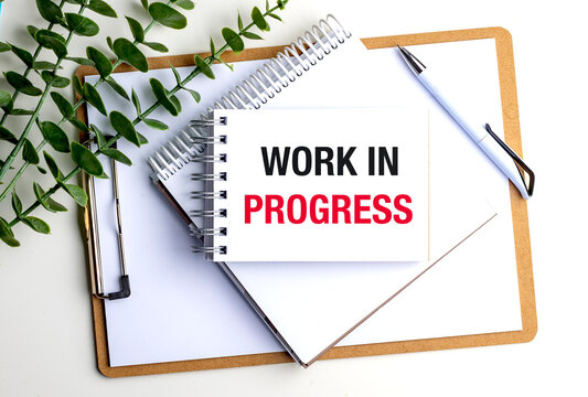 Work in progress concept displayed on notebook with clipboard, pen and green plant on modern office workspace