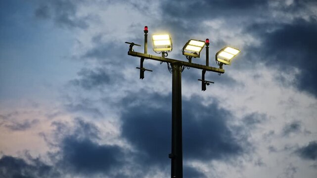View of a tall floodlight mast with lit lamps and red warning beacons against dark storm clouds, Prague, Czech Republic