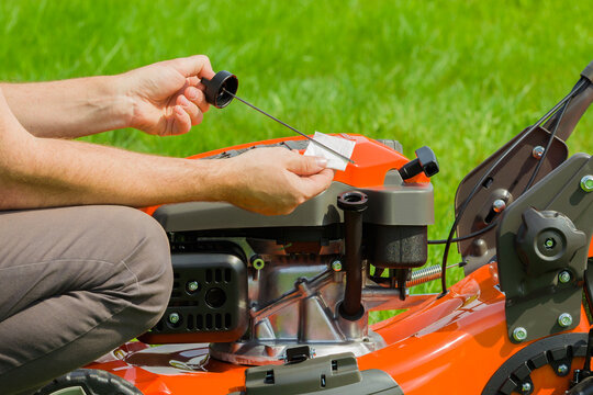 Man hands holding dipstick and white paper and checking oil level of lawn mower on green grass background. Closeup. Side view.