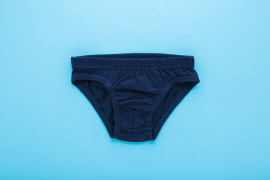 New dark blue panties for little child boy on light blue table background. Pastel color. Closeup. Flat lay. Top down view.