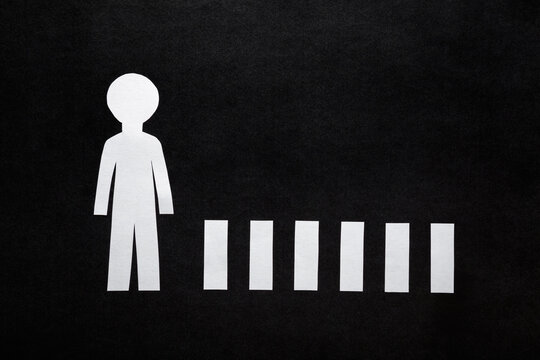 White paper human shape and pedestrian crossing on dark black table background. Closeup. Flat lay. Top down view.