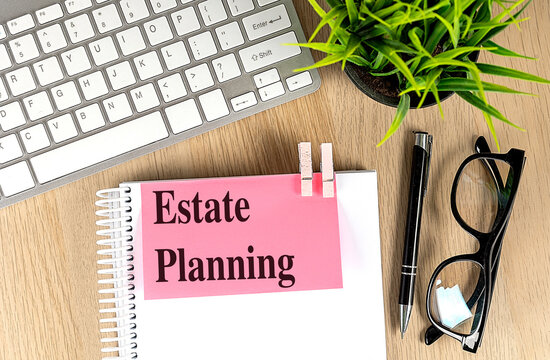 Estate planning concept with notebook, keyboard, pen, eyeglasses and green plant arranged on wooden office desk