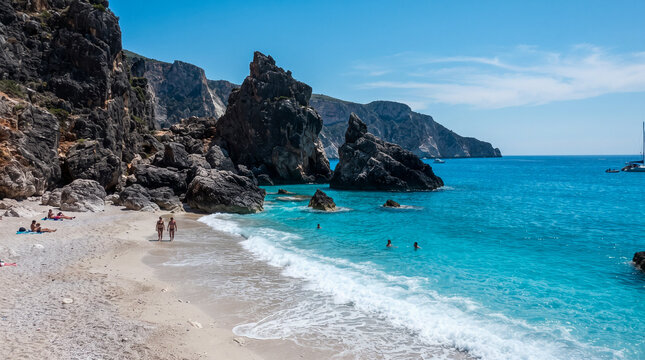 Formaciones rocosas oscuras en un mar azul turquesa, con olas suaves rompiendo en la orilla bajo un cielo despejado. Ideal para turismo y naturaleza.