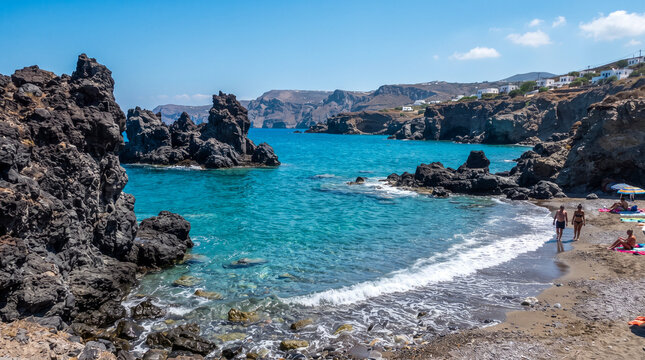 Formaciones rocosas oscuras en un mar azul turquesa, con olas suaves rompiendo en la orilla bajo un cielo despejado. Ideal para turismo y naturaleza.