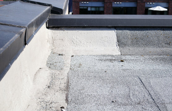 Granule loss on modified bitumen cap sheet. Aggregate pile visible at base. SBS 2-ply roofing system requiring. Maintain and repair flat roof parapet or roofing inspection. Selective focus.