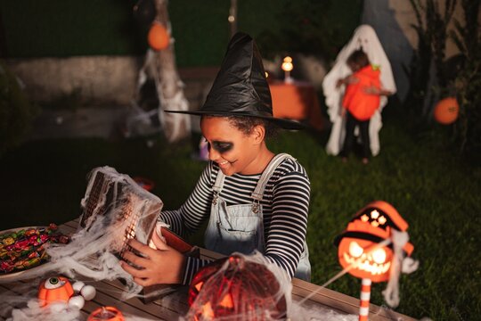 Young girl in witch costume smiling while decorating for a Halloween party in the yard