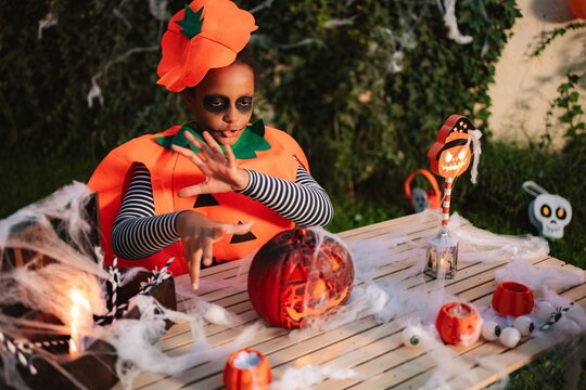 Child in pumpkin costume making magic over Halloween decorations on outdoor table