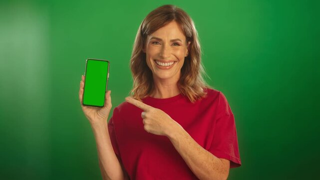 Happy woman in red t-shirt showing smartphone with blank screen on green background for technology promotion