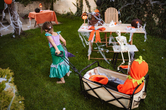 Children playing dress-up, pulling a sibling in a wagon in a decorated backyard for Halloween