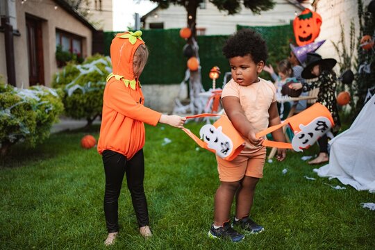 Two children in a pumpkin costume and orange clothes playing with ghost trick or treat bags