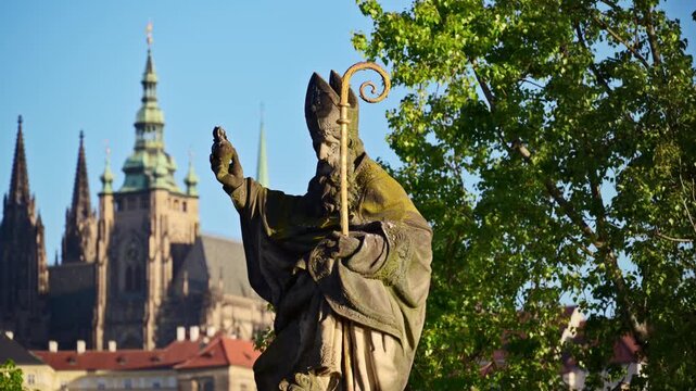 Close-up of a stone statue of a bishop with a gilded crosier, with St. Vitus Cathedral behind, Prague, Czech Republic