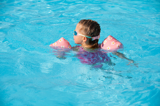 Young Girl Learning to Swim with Arm Floats in Outdoor Pool