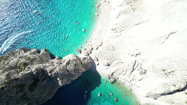 Aerial view of the iconic Navagio Beach with turquoise waters, white limestone cliffs, and small boats anchored in the bay in Zakinthos, Greece.