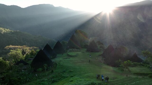 Aerial view of Waerebo Village with its traditional conical houses nestled in lush green mountains during golden hour in Satar Mese Barat, East Nusa Tenggara, Indonesia.