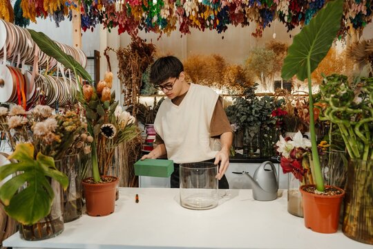 Young male florist holding a supply box in a colorful flower shop