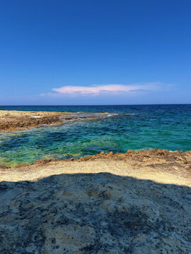 Brilliant turquoise sea meets a rugged rocky shoreline under a vivid blue sky, creating a vibrant summer landscape ideal for snorkeling, travel, coastal tourism and adventure campaigns.