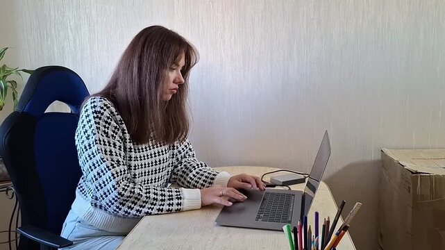 Woman typing on laptop at home desk in a simple room