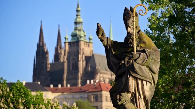 Close-up of a baroque bishop statue on Charles Bridge with St. Vitus Cathedral behind, Prague, Czech Republic