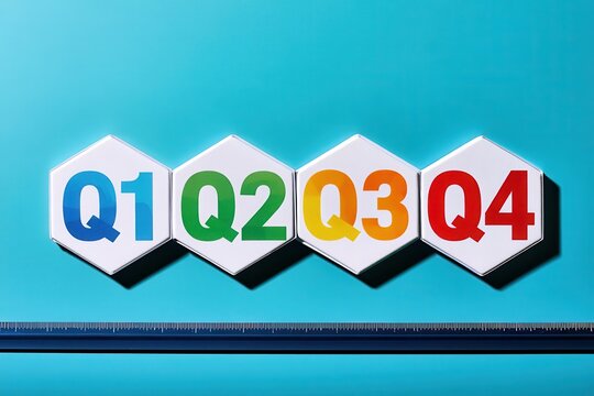 Hexagonal blocks with colorful Q1, Q2, Q3, and Q4 lettering lie in a row on a bright blue surface with a ruler. Perfect for annual business planning and quarterly reporting.