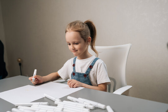 Young child focusing on drawing on white paper with marker pen, expressing creativity and imagination while learning and developing fine motor skills at desk.