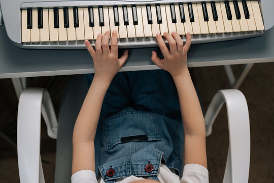 Top down view of young child learning to play musical synthesizer. Kid practicing notes on electronic keyboard at home. Concept of music education, hobby, childhood development.