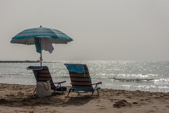 Two beach chairs with umbrella bag and flip flops by the sea