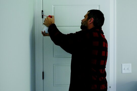 Homeowner applying aerosol silicone lubricant spray grease oil to interior door hinges wiping away residue during routine home maintenance repair work