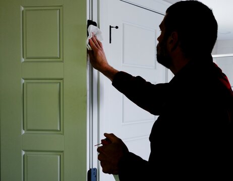 Homeowner applying aerosol silicone lubricant spray grease oil to interior door hinges wiping away residue during routine home maintenance repair work