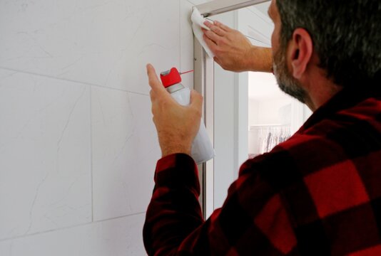 Homeowner applying aerosol silicone lubricant spray grease oil to interior door hinges wiping away residue during routine home maintenance repair work