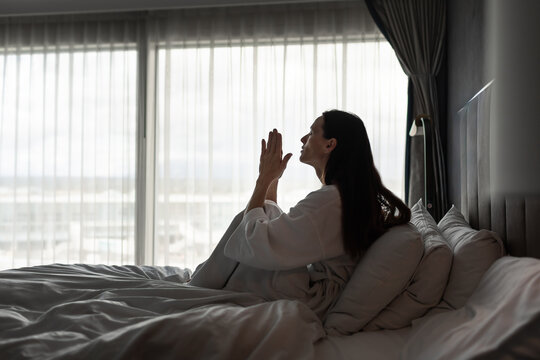 Worried Woman Sitting Alone in Bed Praying for Hope During Stressful Life Crisis
