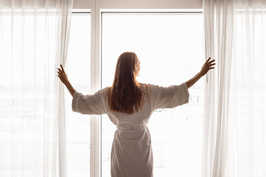 Woman Opening Curtains in Bright Bedroom to Start a Fresh Morning
