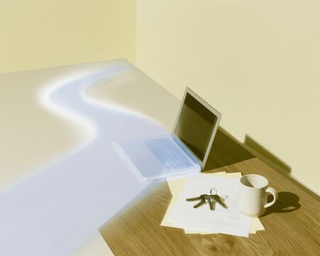 Laptop mockup and house keys on a kitchen table with a glowing digital light path, visualizing the home mortgage process for real estate and banking