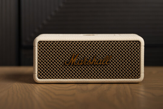 Front view of Marshall Emberton III cream wireless bluetooth speaker with brass grille on wooden table