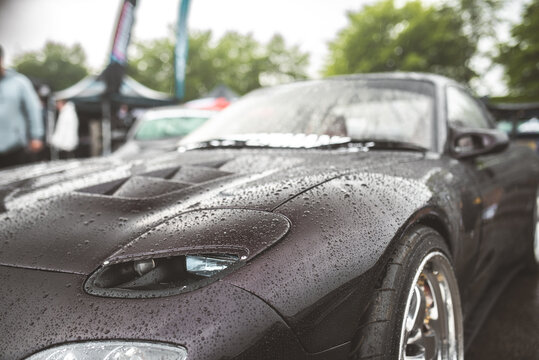 Dark sports car with water droplets on its hood during a rainy day event