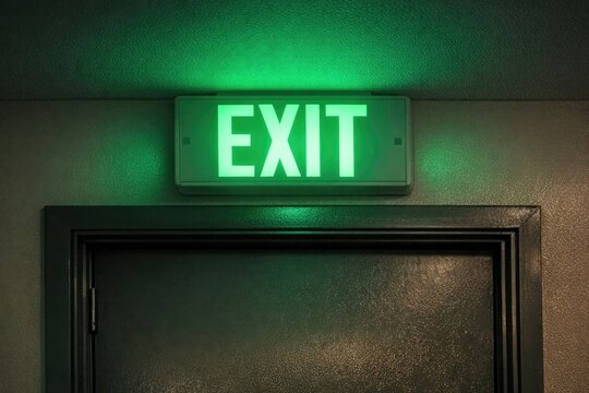A bright green exit sign on the wall of a building, often used as a safety indicator