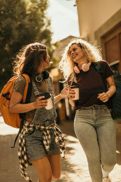 Happy young women walking on street drinking coffee