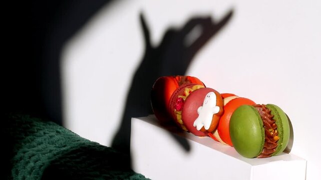 Creative composition of colorful macarons with a hand shadow gesture on a white wall. Halloween. Creative Halloween shot of colorful macarons