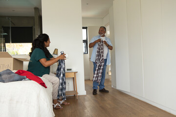 Fototapeta premium African American senior couple packing clothes in bedroom, holding plaid shirts near moving box