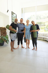 Fototapeta premium Diverse friends standing barefoot in living room holding yoga mats with headphones near glass doors