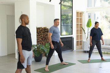 Fototapeta premium Diverse group exercising on green mats in living room including plants and firewood in sportswear