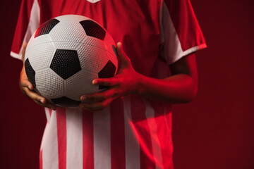 Fototapeta premium African American female holding black-white soccer ball in red-white jersey in red-lit studio