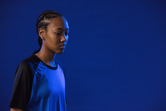African American woman posing on blue backdrop in black-sleeved tee, cornrows, hoops, copy space